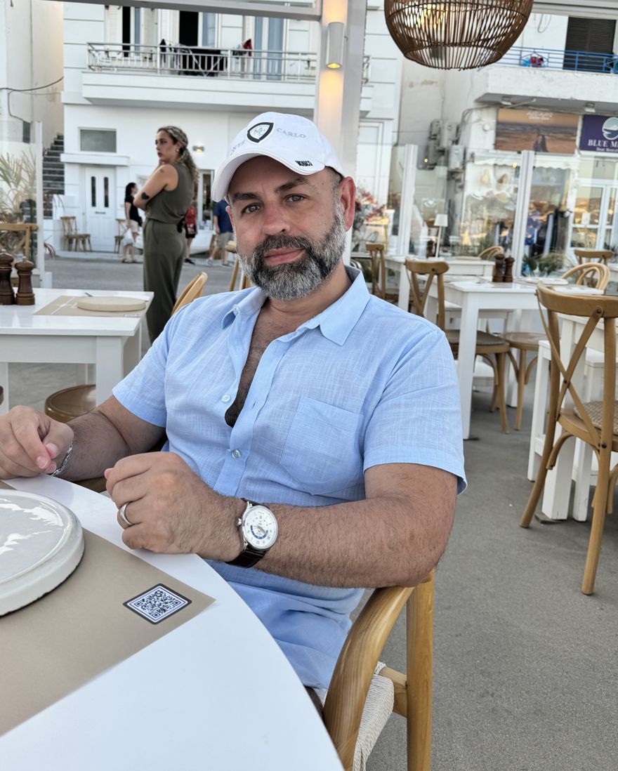 Eliseo Carrillo sitting at a seaside café table in Milos, Greece